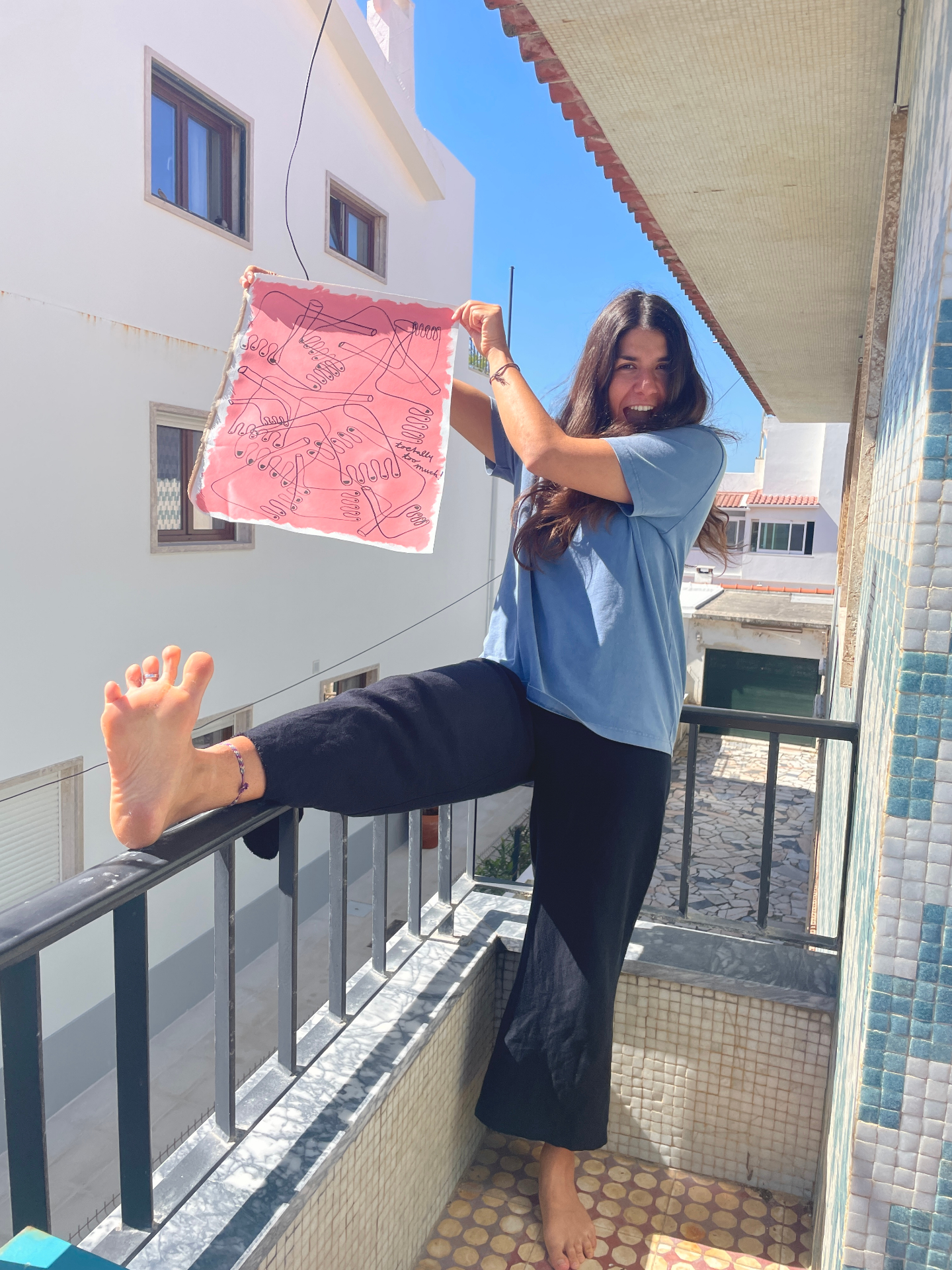 Esrin holding a pink foot painting, stretching her foot toward the camera